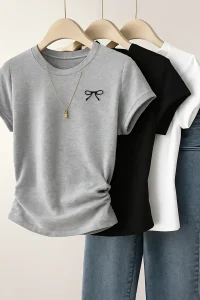 Three T-shirts in gray, black, and white on beige hangers with a gold necklace, paired with blue jeans on a neutral background.