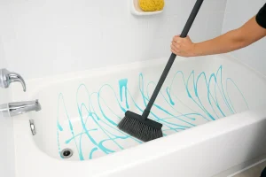 Best bathtub cleaner being spread in a white tub using a broom for deep cleaning.