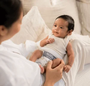 Smiling baby wearing Millie Moon diapers while resting with parent.